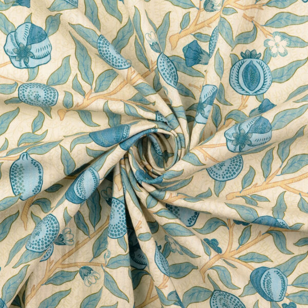 Gefalteter Baumwollstoff mit blauem Granatapfel-Muster auf beigem Hintergrund, in dekorativer Spirale gelegt, sichtbar strukturierte Popeline-Webart.