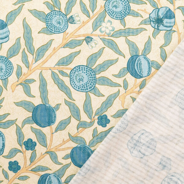 Baumwollstoff mit blauem Granatapfel-Motiv auf Beige, Vorderseite vollständig sichtbar, untere Ecke umgeklappt und Rückseite mit matter Struktur gezeigt.