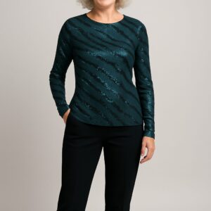 Startseite Ältere Frau mit lockigem weißem Haar trägt ein elegantes, langärmliges Oberteil aus grünem Jersey-Modestoff mit Paillettenmuster. Sie steht lächelnd und selbstbewusst, kombiniert das Oberteil mit einer schwarzen Stoffhose.